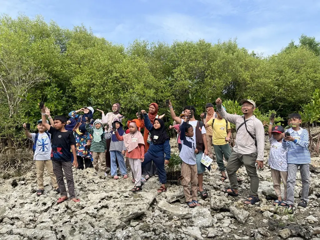 Anak-anak dan pendamping mengangkat bibit mangrove sebelum menanam
