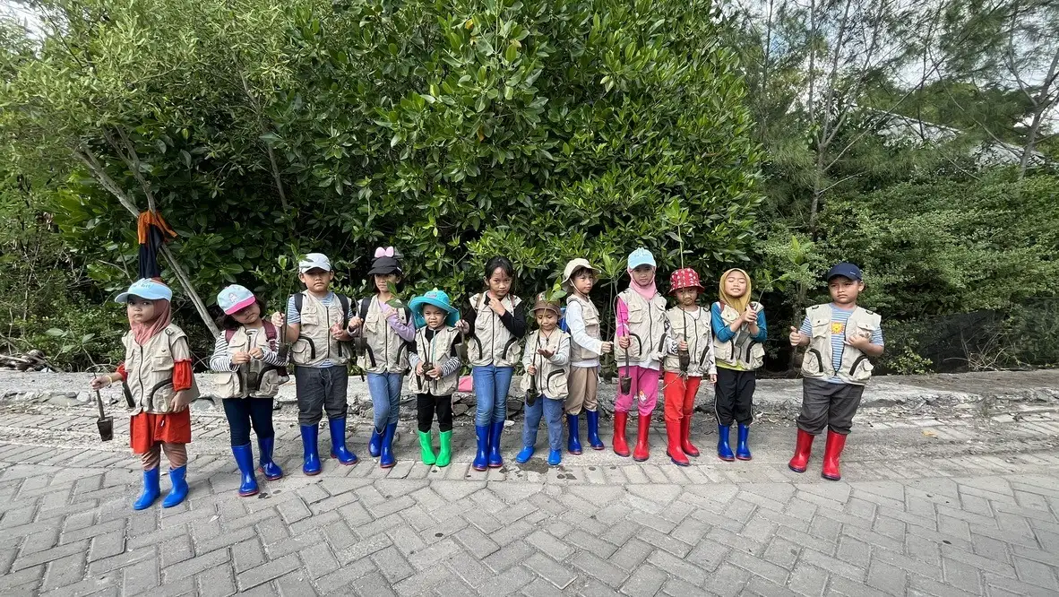 Anak-anak bersepatu bot berbaris membawa bibit mangrove